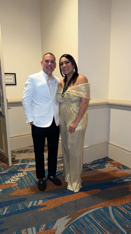 Smiling couple at a gala, the woman in a gold pleated evening gown
